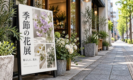 花店の入口に置かれた白地に濃い文字の看板と白い花｜誉PRINTING